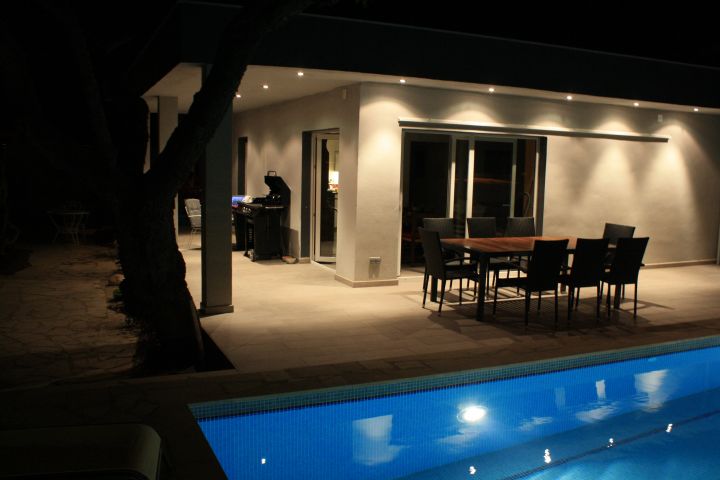 Blick über den beleuchteten Pool auf die 50m2 grosse Terrasse des Casa El Almendro bei Nacht 